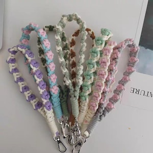 May include: A collection of six macrame wristlet lanyards featuring knotted cord designs in various pastel colors including purple, pink, blue, green, brown, and gray, each finished with a silver-toned metal lobster clasp at the bottom end.