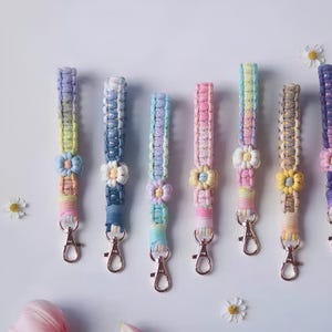 May include: Seven colourful crocheted keychains with flower accents and gold key rings. The keychains are made with a variety of pastel colours, including pink, blue, yellow, and green.
