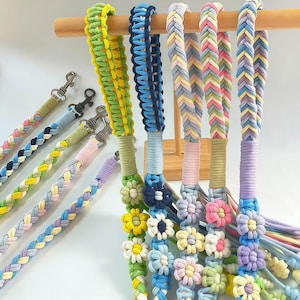 Puede incluir: Una colección de cordones trenzados coloridos con cierres metálicos. Los cordones presentan varios patrones y colores, incluyendo verde, azul, amarillo, rosa y morado. Algunos cordones están adornados con adornos en forma de flor.