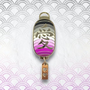 Może przedstawiać: Złota metalowa przypinka w kształcie japońskiej latarni z tęczowym gradientem i chińskim znakiem miłości "愛" w kolorze złotym. Latarnia ma mały złoty urok z dwoma sercami zwisającymi z niej.