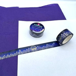 Op de afbeelding: Een rol washi tape met een zwarte achtergrond en gouden accenten. De tape heeft een herhalend patroon van bergen, sterren en een zon. De tape is gelabeld "Synthwave Mountains" en is verpakt in een doorzichtige plastic container.