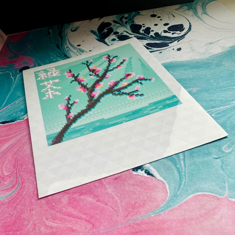 May include: A white card with a pixelated image of a pink cherry blossom tree on a blue background. The text "桜茶" is printed in black on the card.