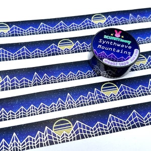 Op de afbeelding: Een rol washi tape met een blauw en wit geometrisch bergontwerp en een gele zon. De tape is gelabeld met "Synthwave Mountains" en "washi tape" met een konijnenlogo.