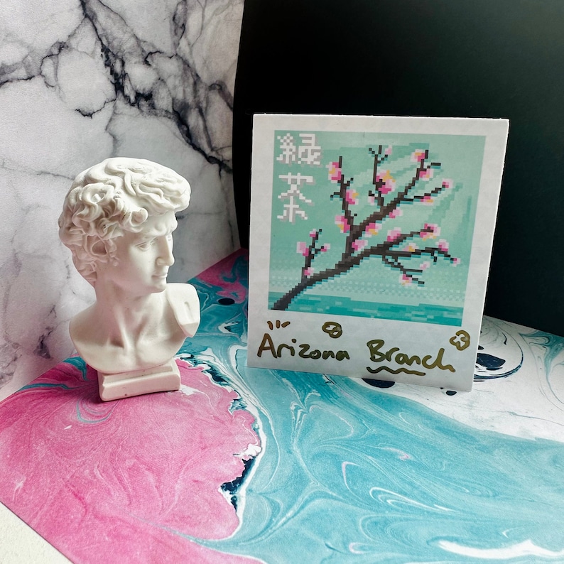 May include: A white plaster bust of a man with a white background. A white card with a pixelated image of a pink cherry blossom tree on a blue background. The card has the text "Arizona Branch" written on it in gold.