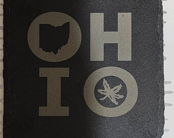 Könnte beinhalten: Schwarzer Schieferuntersetzer mit dem Wort "OHIO" in weißen Buchstaben. Die "O"s sind durch eine Umrandung des Bundesstaates Ohio und ein stilisiertes Ahornblatt ersetzt.