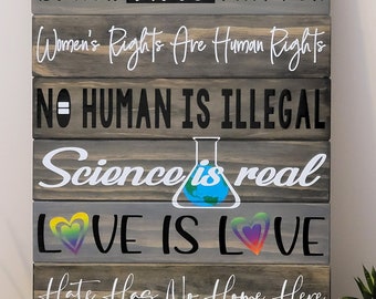 May include: A wooden sign with the text "In this house we believe... BLACK LIVES MATTER Women's Rights Are Human Rights NO HUMAN IS ILLEGAL Science is real LOVE IS LOVE Hate Has No Home Here INJUSTICE Anywhere Is A Threat To Justice Everywhere - MLK"