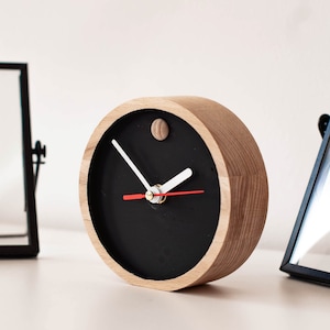 May include: A wooden clock with a black face and white hands. The clock has a simple design and is perfect for a modern home.