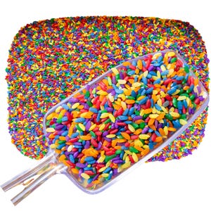 May include: A clear plastic scoop filled with colorful rainbow rice. The rice is scattered around the scoop, creating a vibrant and playful scene.