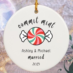 May include: A white ceramic ornament with a gold string for hanging. The ornament features the words "commit mint" above a candy graphic with red, pink, and green stripes. Below the candy is "Ashley & Michael married 2025."