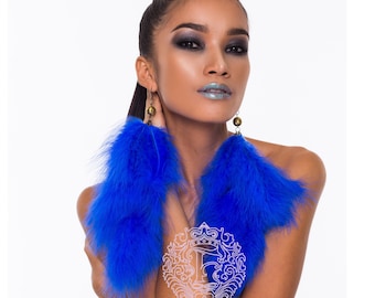 May include: A pair of long, blue feather earrings with gold accents. The earrings are worn by a person with dark hair and makeup.