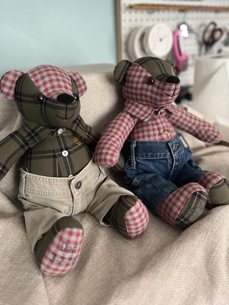 Op de afbeelding: Twee handgemaakte teddyberen gemaakt van geruite stof. De linkerbeer draagt een groen geruit overhemd en een beige broek, met 'Dad 3-7-22' op de voet geborduurd. De rechterbeer draagt een rood geruit overhemd en een blauwe spijkerbroek.