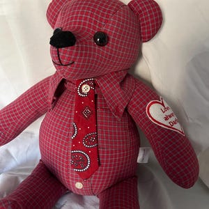 Op de afbeelding: Een knuffelbeer gemaakt van rood-witte ruitjesstof. De beer heeft een rode das met paisleyprint en een klein wit knoopje, zwarte plastic ogen, een zwarte neus en een wit hartvormig embleem op de arm met de tekst Love always Dad.