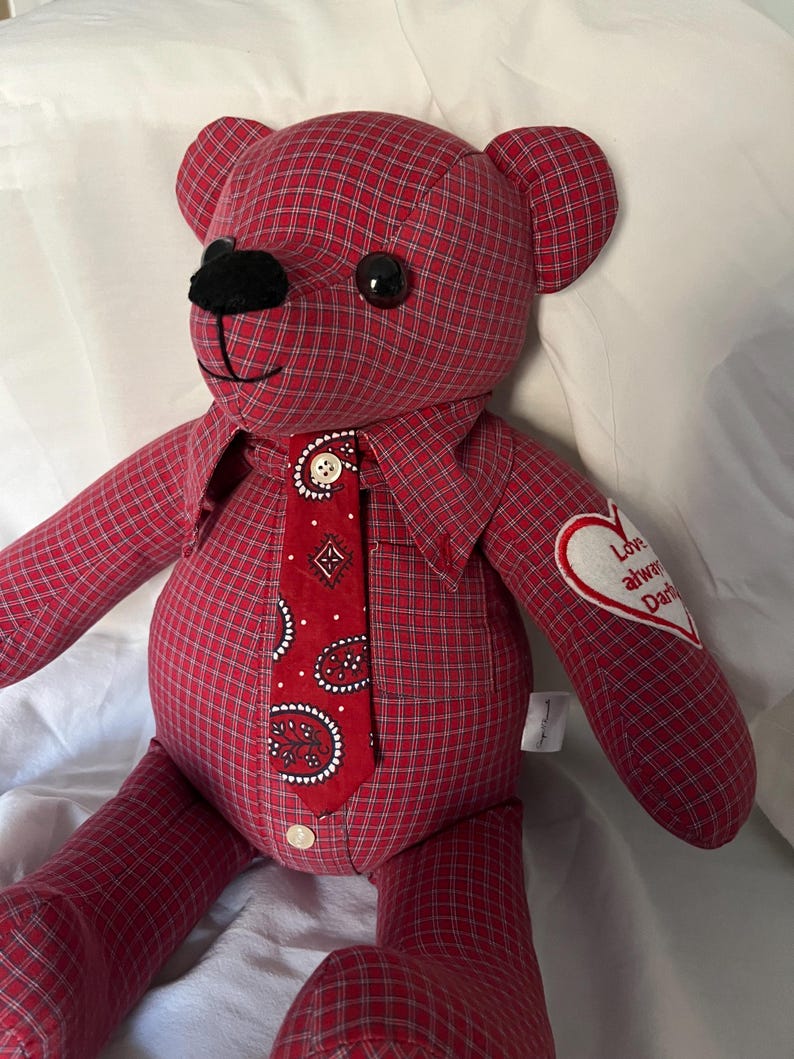 Op de afbeelding: Een knuffelbeer gemaakt van rood-witte ruitjesstof. De beer heeft een rode das met paisleyprint en een klein wit knoopje, zwarte plastic ogen, een zwarte neus en een wit hartvormig embleem op de arm met de tekst Love always Dad.