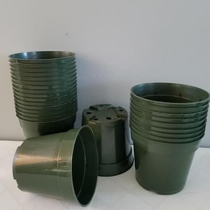 May include: A stack of dark green plastic plant pots. The pots are stacked in a pile, with some of the pots laying on their side.