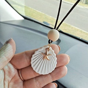May include: White ceramic seashell car charm with a gold starfish accent hanging from a black string with a wooden bead.