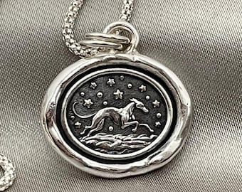 May include: A silver necklace with a round pendant featuring a stylized greyhound running across a field of stars. The pendant has a textured, aged look.