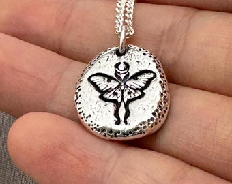 May include: Silver necklace with a round pendant featuring a detailed engraved image of a moth with wings spread.