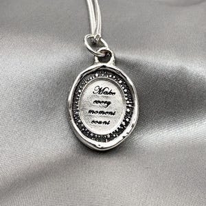 May include: Silver pendant necklace with a round, textured charm that says "Make every moment count".