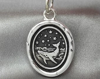 May include: A silver pendant necklace with a whale and stars design. The whale is jumping out of the water and there are stars in the sky above it.
