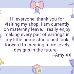 May include: A light blue card with a white border and a message that reads "Hi everyone, thank you for visiting my shop, I am currently on maternity leave. I really enjoy making every pair of earrings in my little home studio and look forward to creating more lovely designs in the future. --Amy XX". The card is decorated with various baby-themed illustrations, including a pacifier, a rattle, a baby bottle, a duck, and a baby carriage.