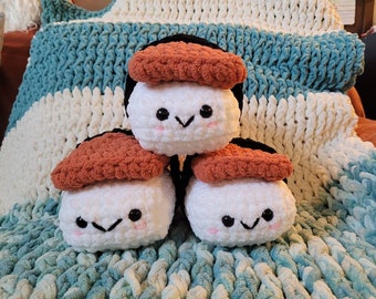 May include: Three crocheted sushi plush toys. The sushi is made of white yarn with a brown topping and black seaweed. Each sushi has a cute face with black eyes and a smiling mouth.