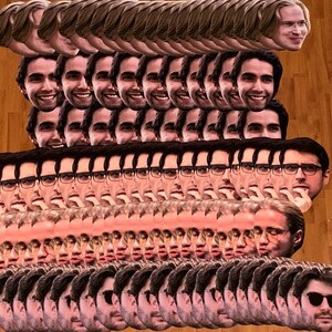 May include: A large stack of paper face masks featuring a man's face. The masks are arranged in rows and columns, with the man's face facing forward in each mask. The masks are printed on white paper and have a realistic appearance.