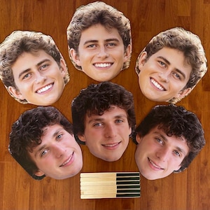 May include: Six paper face masks of young men with brown hair. The masks are printed with realistic images of the men's faces.