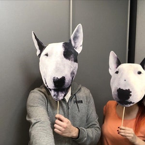 May include: Two people are holding up cardboard cutouts of bull terrier dog faces. The cutouts are on sticks. The person on the left is wearing a gray sweatshirt with the word "Puma" on the front. The person on the right is wearing an orange shirt.