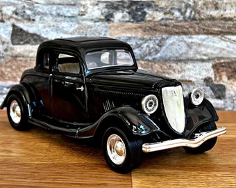 May include: A black vintage car model with chrome accents. The car has a rounded body style and a classic grille.