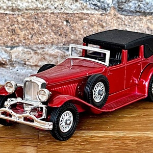 May include: A red vintage car model with a black convertible top. The car has chrome accents and whitewall tires.
