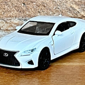 Op de afbeelding: Een witte Lexus RC F modelauto met zwarte wielen en afwerking. De miniatuur coupé heeft een gedetailleerde grille en koplampen. De auto staat op een houten oppervlak.