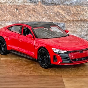 Könnte beinhalten: Ein rotes Spielzeugautomodell eines Audi e-tron GT, einer leistungsstarken elektrischen Limousine. Das Auto hat schwarze Räder und ein schwarzes Dach.