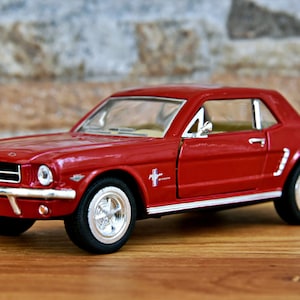 May include: A red toy car model of a classic Ford Mustang. The car has a black interior and chrome accents. The car is sitting on a wooden surface.