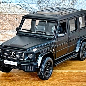 Può includere: Modello di auto Mercedes-Benz Classe G AMG nero con una griglia nera e un logo Mercedes argentato. L'auto ha ruote nere e un interno nero.