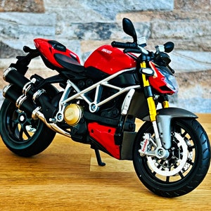 Peut inclure: Modèle de moto Ducati rouge avec des roues et des pots d'échappement noirs. La moto a un cadre argenté et des accents dorés.