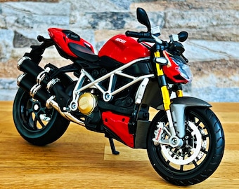 May include: A red Ducati motorcycle model with black wheels and exhaust pipes. The motorcycle has a silver frame and gold accents.