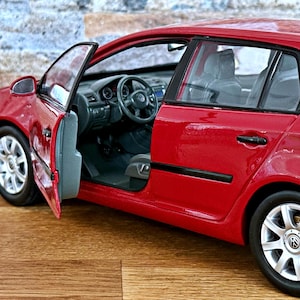 May include: A red model car with the driver's side door open, revealing the interior. The car has silver rims and a black interior. The car is sitting on a wooden surface.