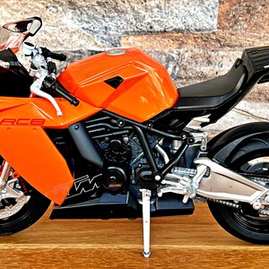 May include: Orange and black motorcycle model with the text "RC8" on the side. The motorcycle is on a wooden surface.