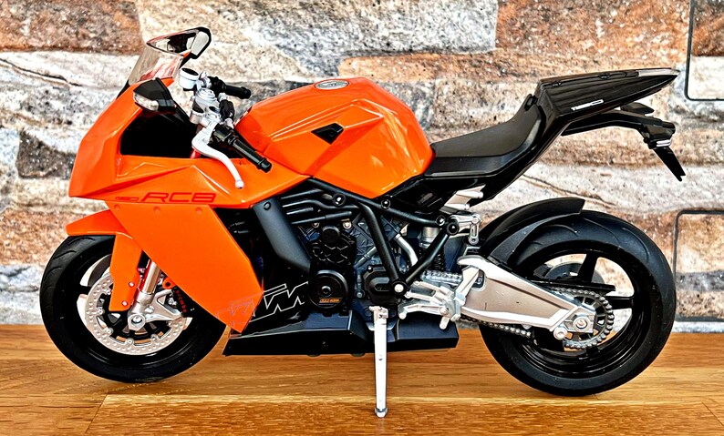 May include: Orange and black motorcycle model with the text "RC8" on the side. The motorcycle is on a wooden surface.