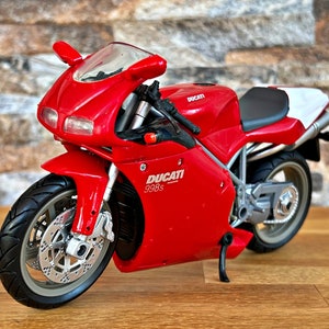 Peut inclure: Modèle de moto Ducati 998s rouge. La moto a une selle blanche et des accents noirs.