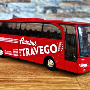 May include: A red toy bus with the words "Autobus Travego" and "Super Coach" printed on the side. The bus has black windows and a detailed front grill.