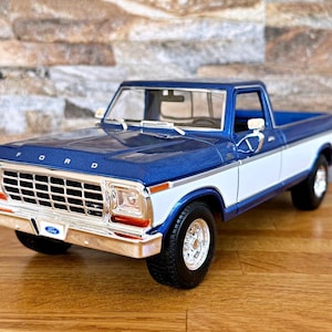 Pode incluir: Um modelo de pick-up Ford azul e branco. O camião tem cabine e capô azuis, com carroçaria branca. A grelha dianteira é cromada e os pneus são pretos.
