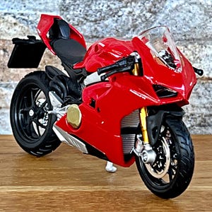 Peut inclure: Modèle de moto rouge et noire avec un pare-brise transparent. La moto a une selle noire et un pot d'échappement argenté.