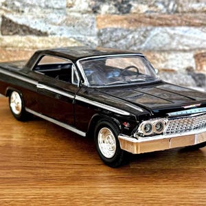 Könnte beinhalten: Ein schwarzes Druckguss-Modellauto mit einem verchromten Frontgrill, silberfarbenen Stoßstangen und weiß umrandeten Rädern. Das Fahrzeug hat eine zweitürige Coupé-Karosserie mit klaren Fenstern, die einen detaillierten Innenraum zeigen.