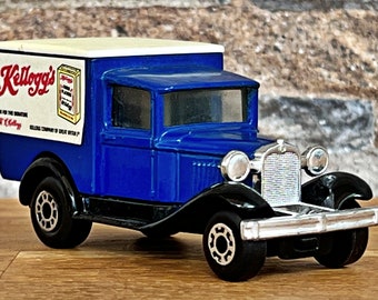 May include: A die-cast model of a vintage blue Kellogg's delivery truck. The truck features a white roof and the Kellogg's logo on the side. The model has black tires and silver accents, and is a collectible item.