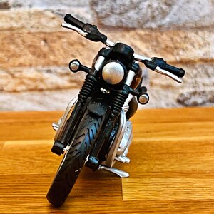 May include: Black toy motorcycle with a silver headlight and chrome accents. The motorcycle is on a wooden surface.