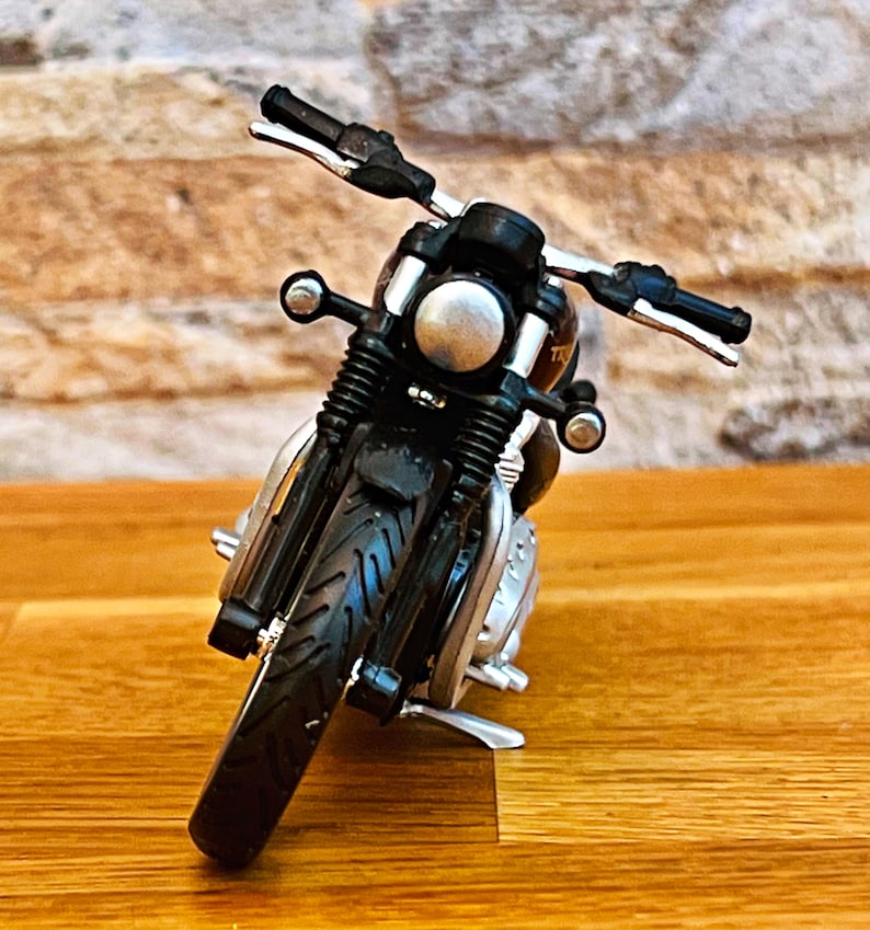 May include: Black toy motorcycle with a silver headlight and chrome accents. The motorcycle is on a wooden surface.