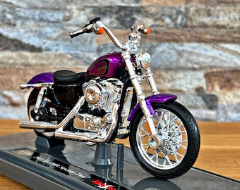 Pode incluir: Um modelo de motocicleta roxo e cromado com motor e rodas detalhados. O modelo está em um suporte de exibição com o texto "Harley-Davidson Sportster Two" impresso na base.