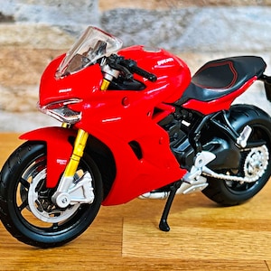 Peut inclure: Modèle de moto Ducati rouge avec des accents noirs et un pare-brise transparent. La moto est sur une surface en bois.