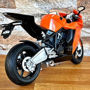 May include: Orange and black motorcycle model with the KTM logo on the side and tail. The motorcycle has a silver exhaust pipe and black wheels.